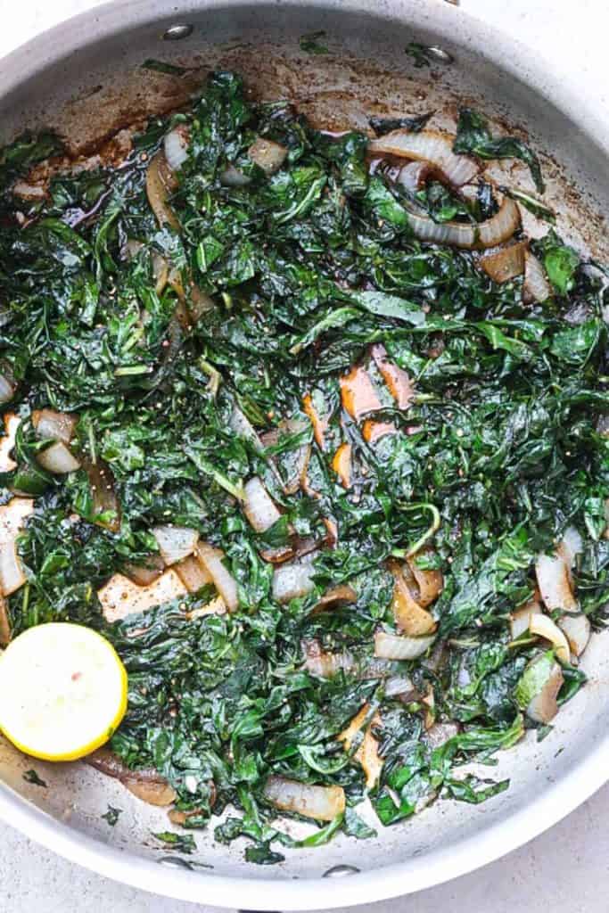 collard greens and onions sauted in a pan with fresh lemon halves