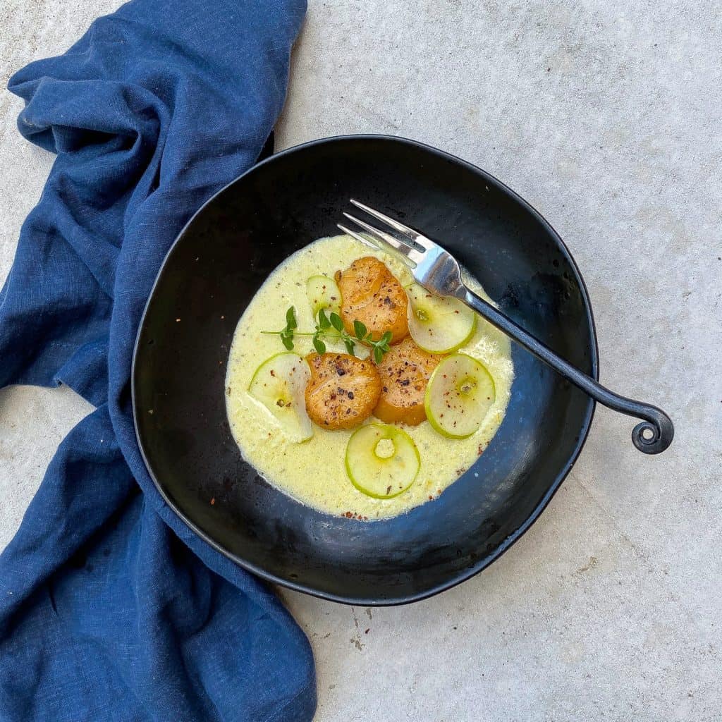 smoked scallops in black bowl with sauce