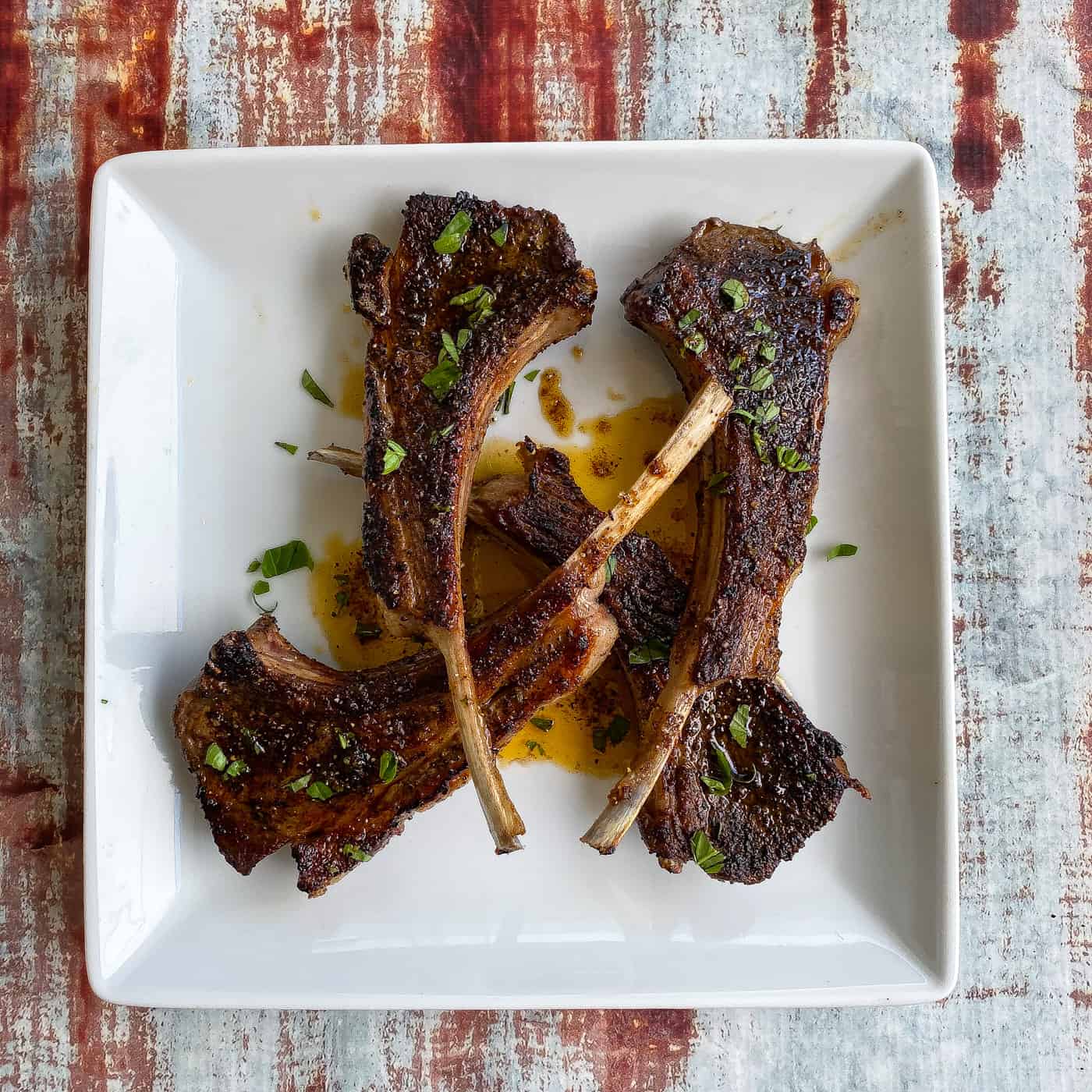 coffee rubbed broiled lamb chops on a white plate with green herbs
