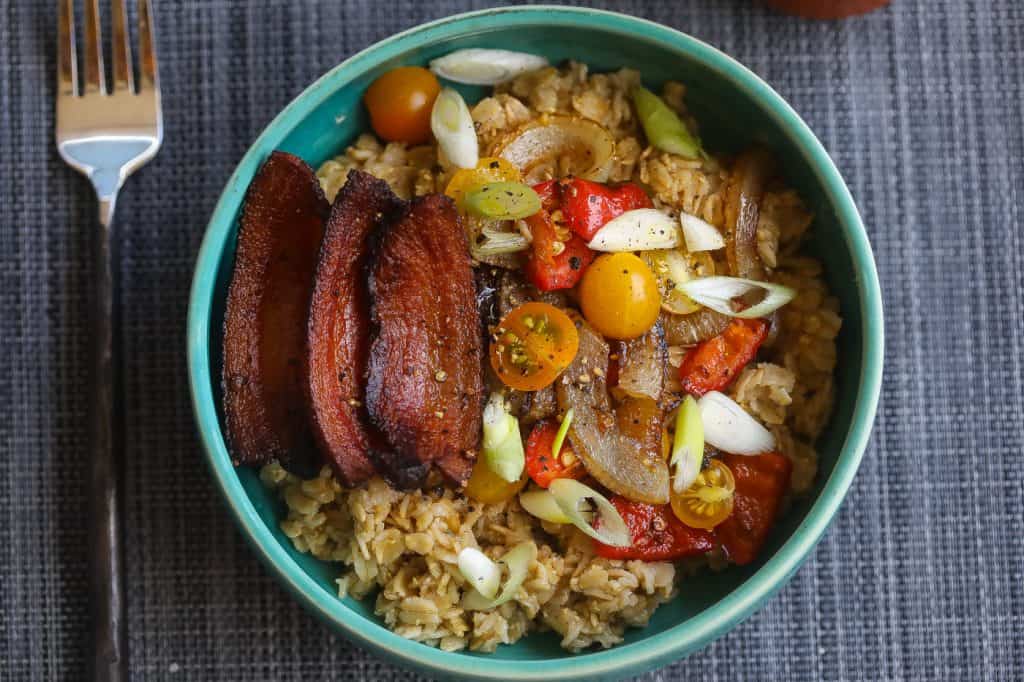 oatmeal topped with bacon and vegetables in a blue bowl