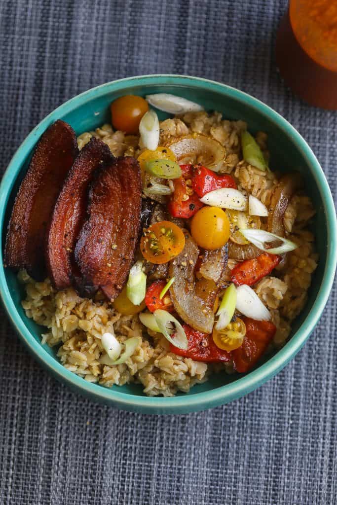 oatmeal topped with bacon and vegetables in a blue bowl