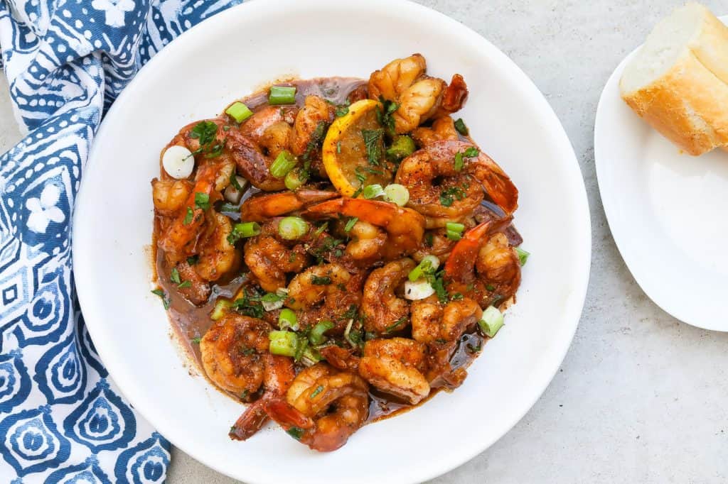 bbq shrimp on a white plate with green onions and parsley