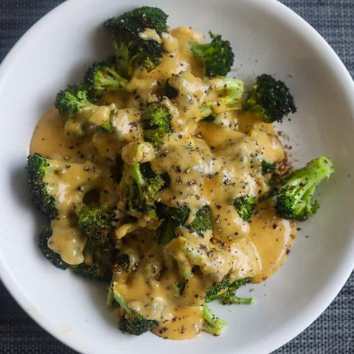 broccoli topped with cheese sauce on white plate