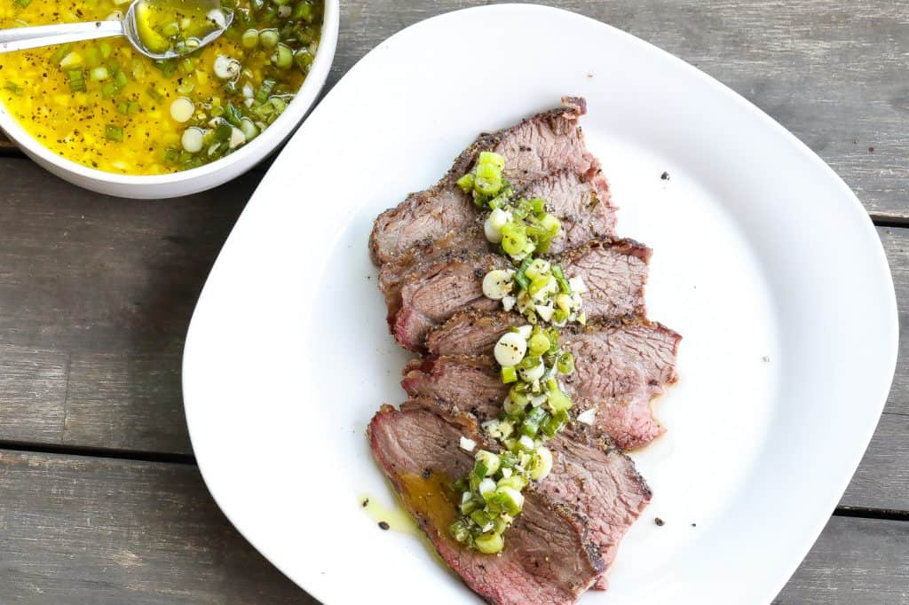 smoked tri tip topped with green sauce on a white plate