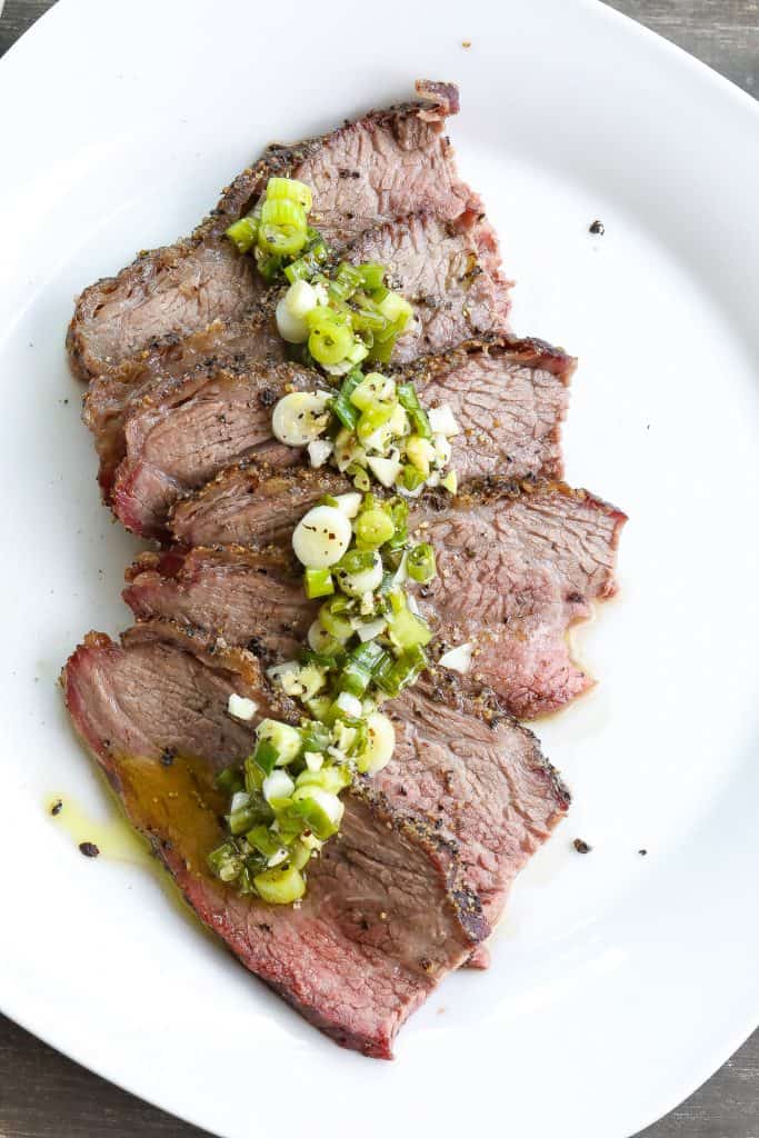 smoked tri tip topped with green sauce on a white plate