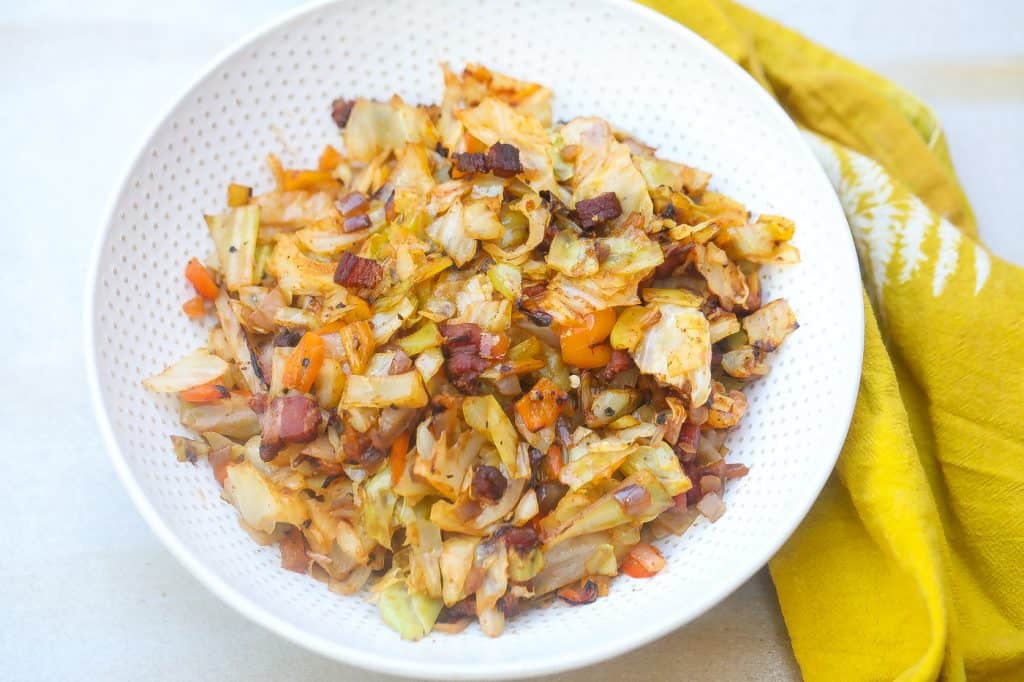 Fried cabbage and bacon on a white plate