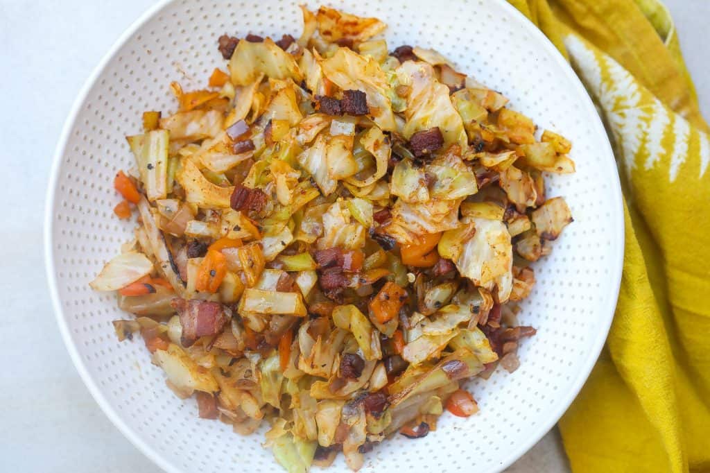 Fried cabbage and bacon on a white plate