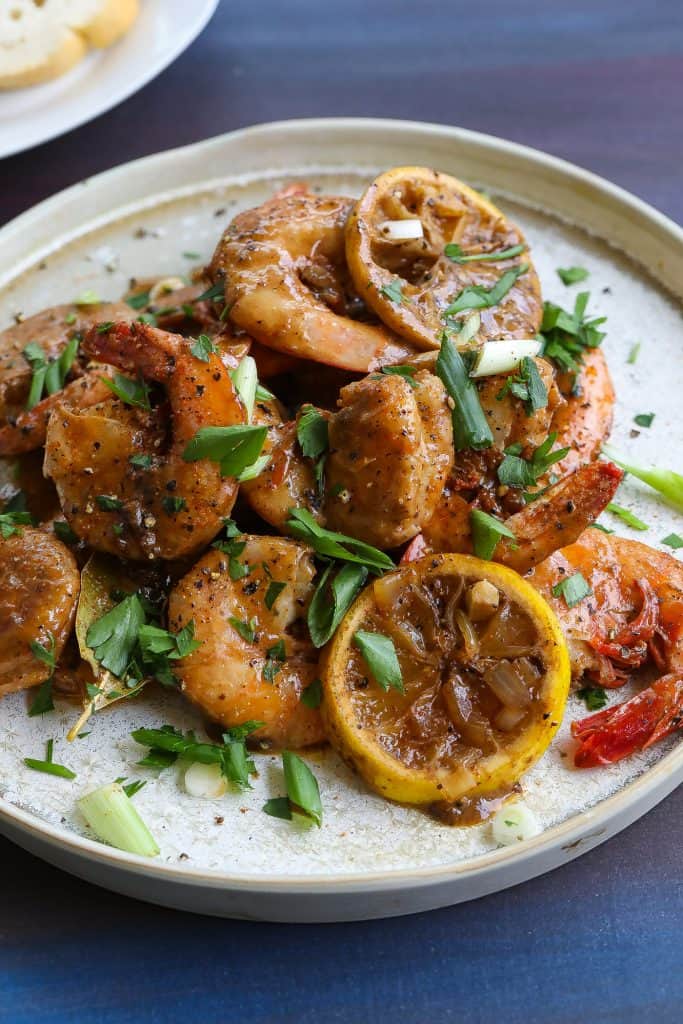 bbq shrimp on a plate topped with parsley, green onions, and lemons