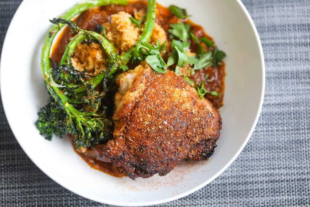 crispy chicken thighs with broccoli and fonio grain in white bowl