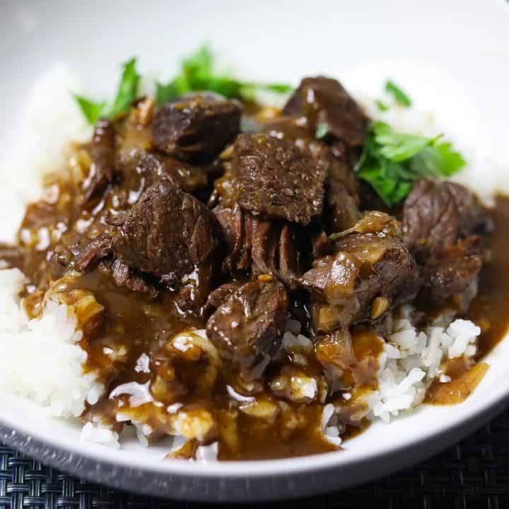 beef tips and rice topped with gravy in a white bowl