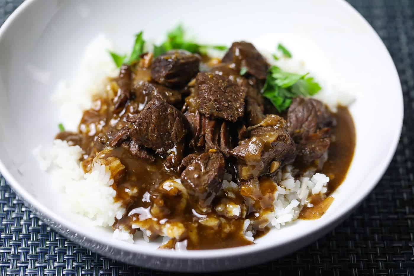 beef tips and rice topped with gravy in a white bowl