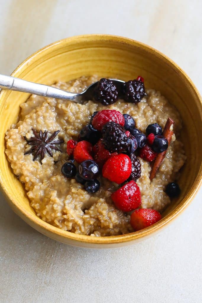 cinnamon oatmeal in yellow bowl with spices and berries