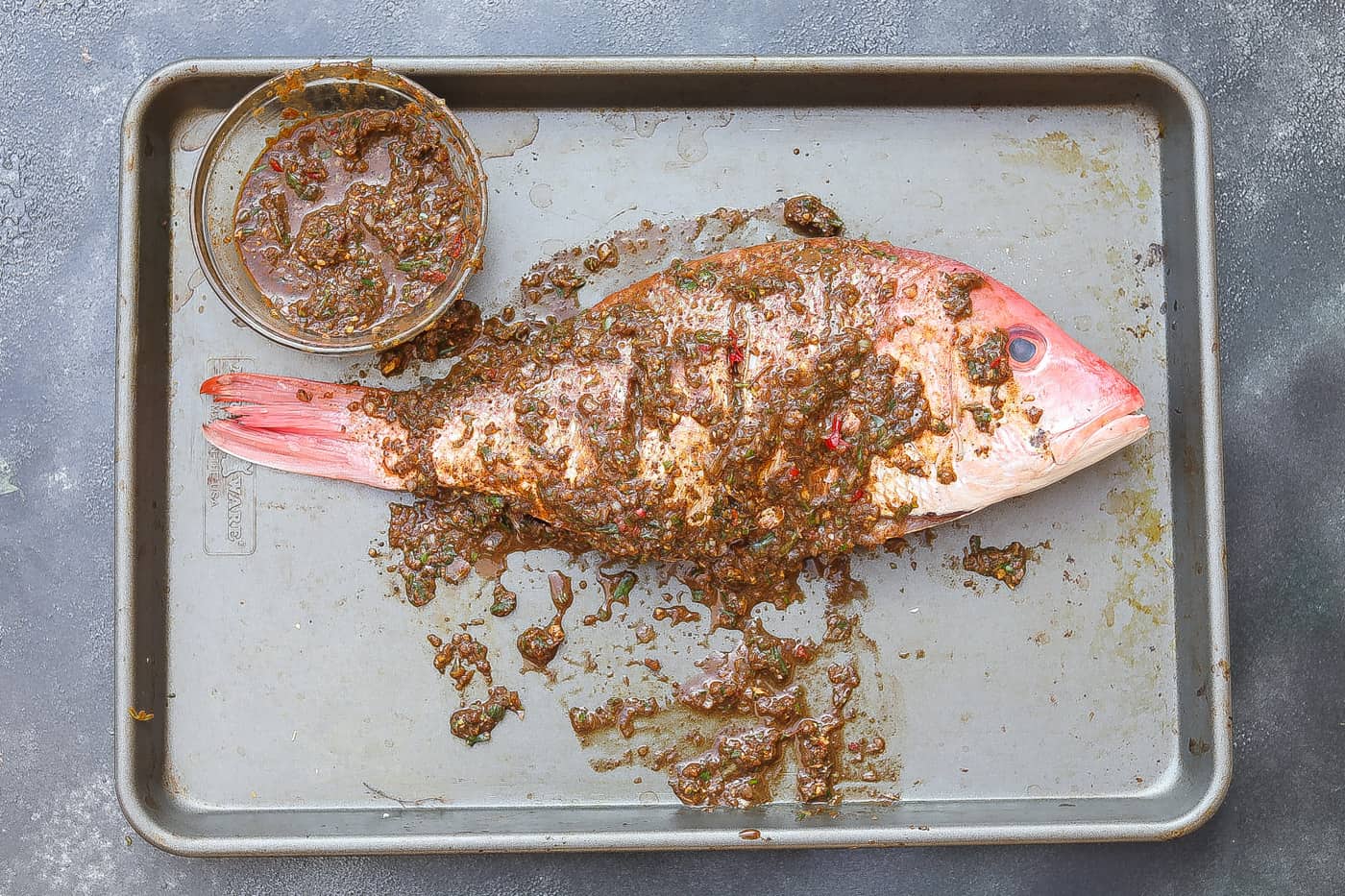 whole raw red snapper covered by jerk marinade on a tray