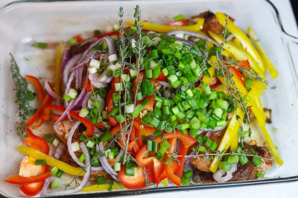 chicken marinating under peppers and onions