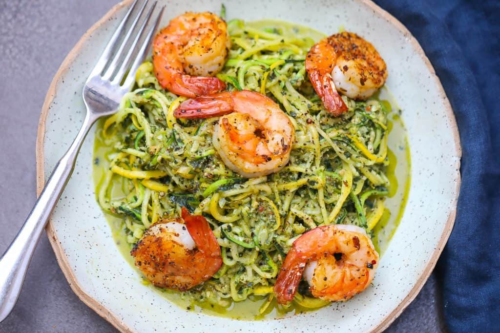 zoodles with pesto topped with shrimp on green plate