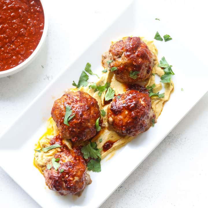 meatballs sitting on top of hummus on white plate