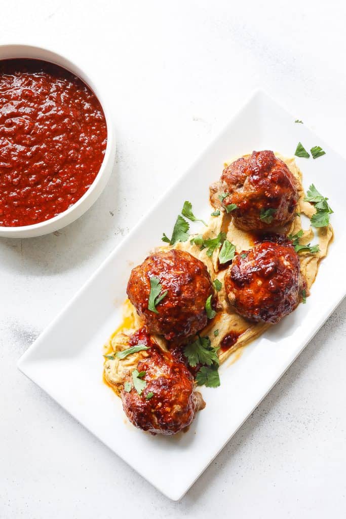 meatballs sitting on top of hummus on white plate