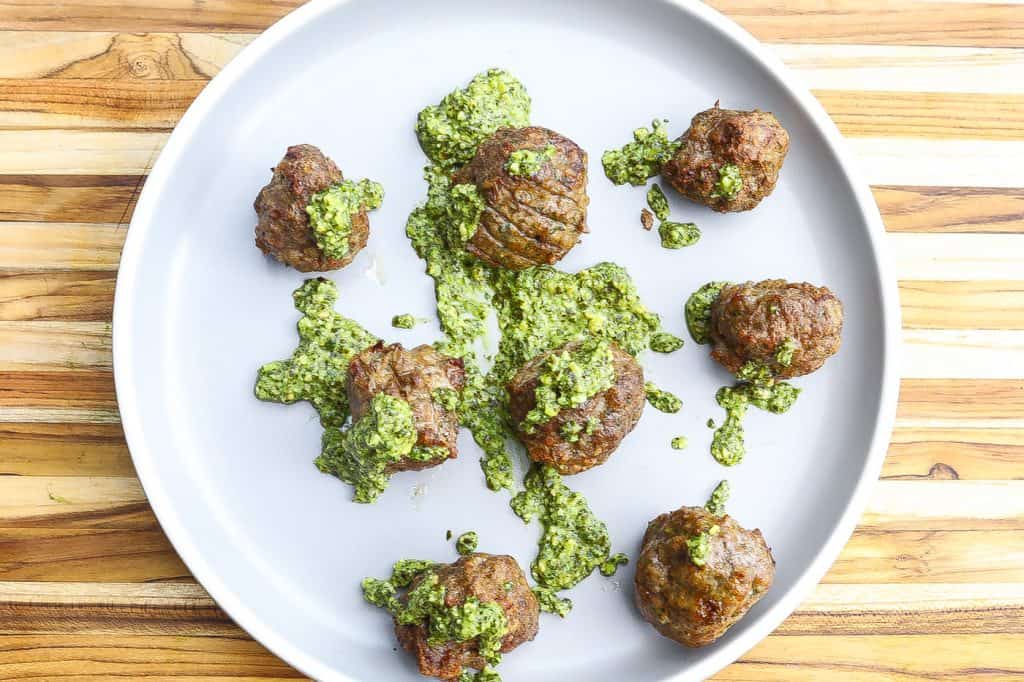 lamb meatballs on a grey plate topped with pesto