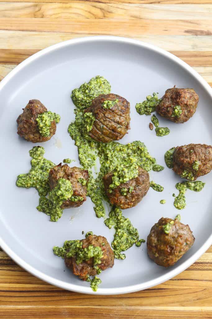 lamb meatballs on a grey plate topped with pesto