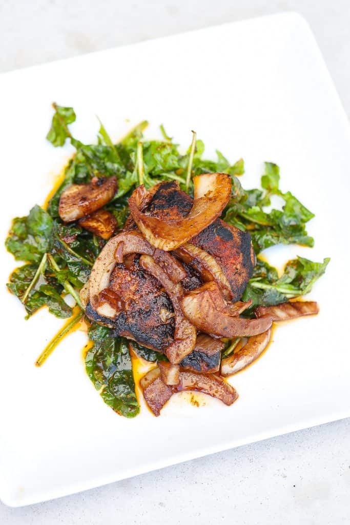 pork steak topped with onions on a white plate with greens