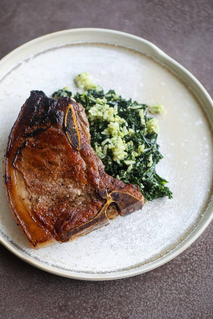 pork chop on top of spinach on tan plate