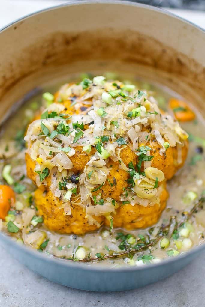 whole yellow cauliflower in pan topped with leeks and green onions