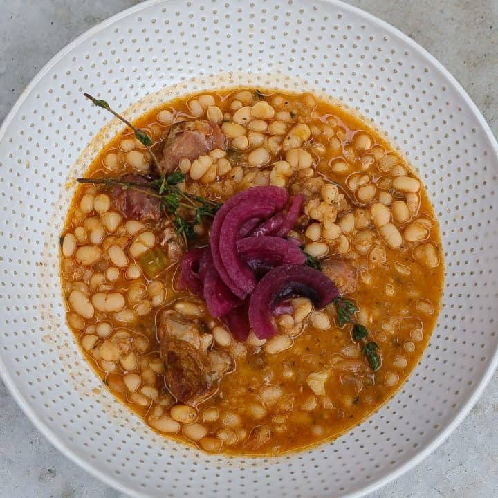 navy beans and ham in a white bowl topped with red onions
