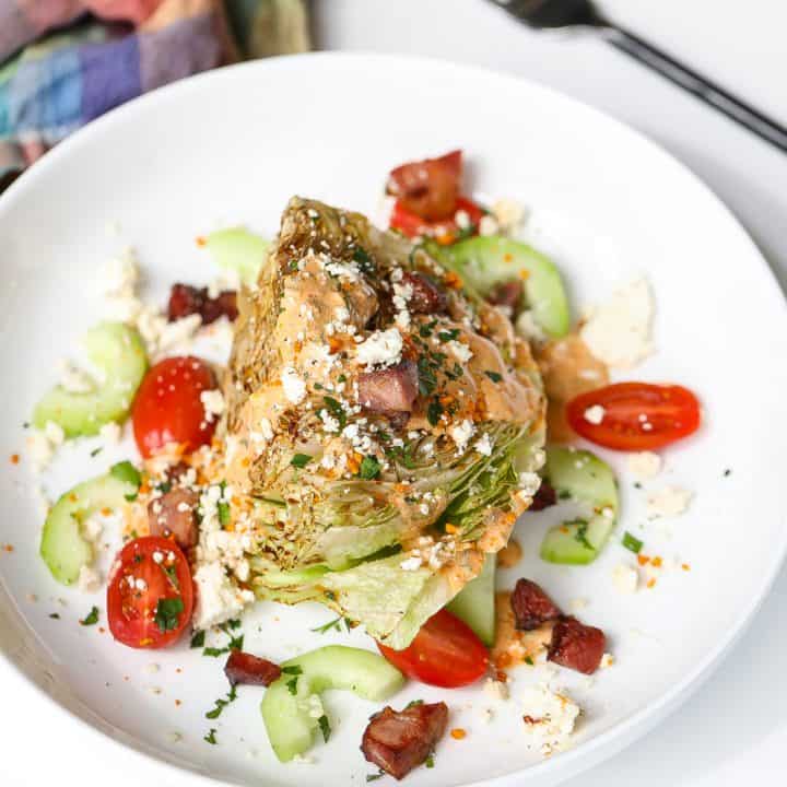 wedge salad on white plate with tomatoes and dressing