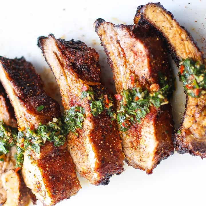 babyback ribs on a white plate topped with chimichurri sauce