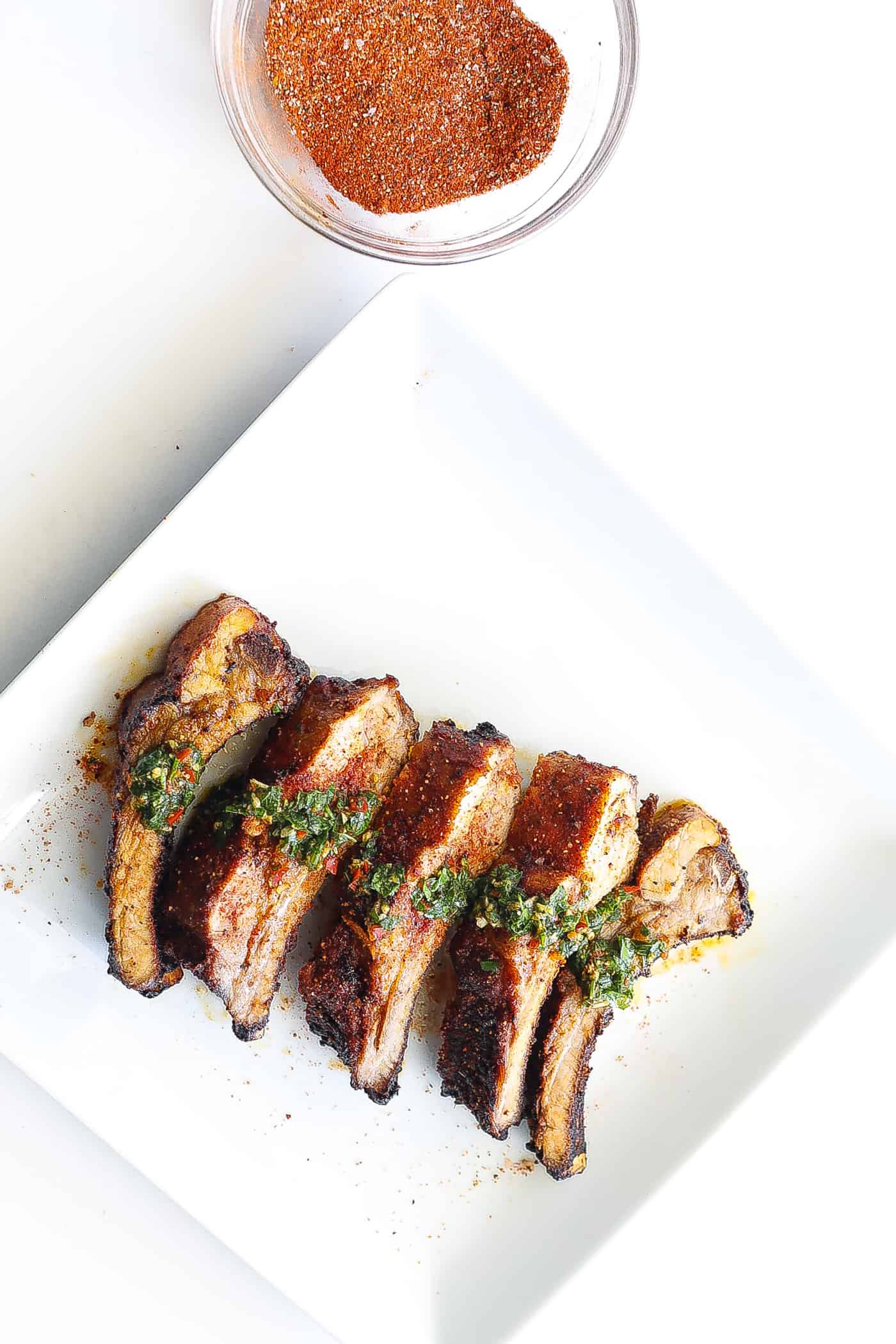 babyback ribs on a white plate topped with chimichurri sauce