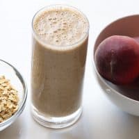 oatmeal smoothie in a tall glass with peaches and oats on the side
