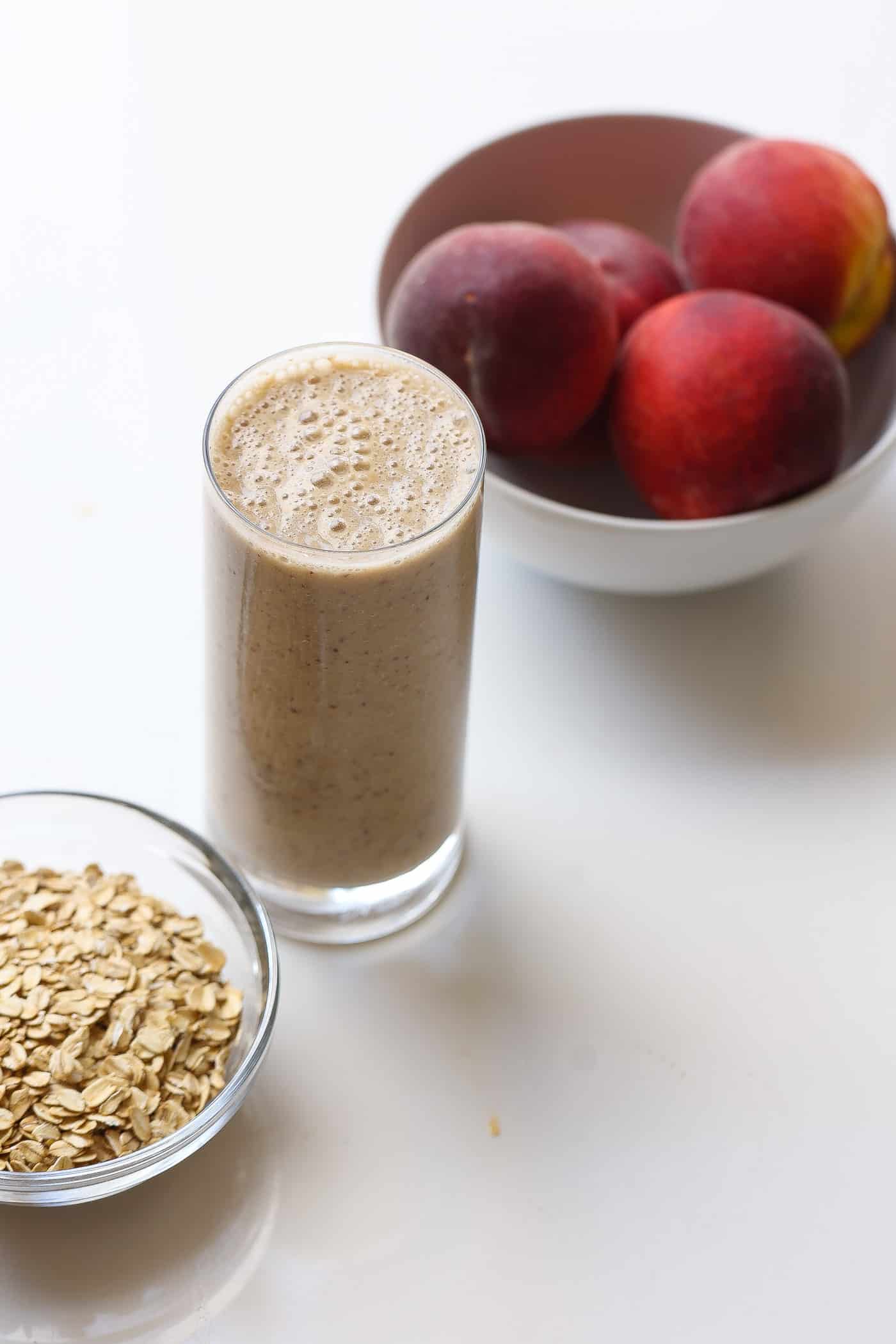 oatmeal smoothie in a tall glass with peaches and oats on the side