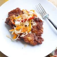 fried pork steak on white plate topped with slaw