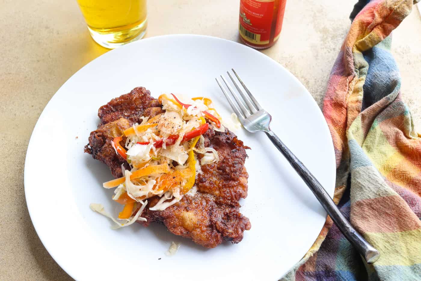 fried pork steak on white plate topped with slaw