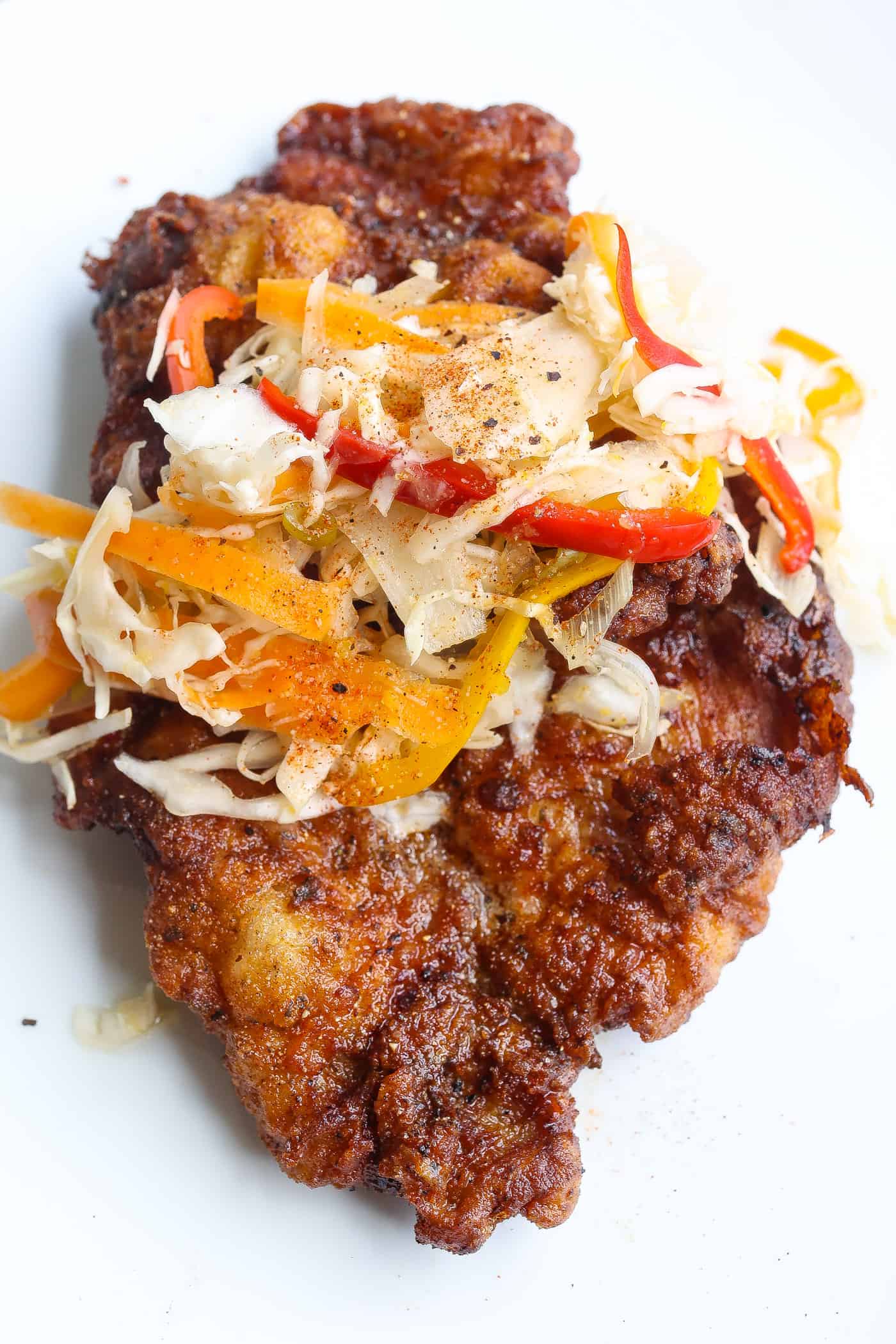 fried pork steak on white plate topped with slaw