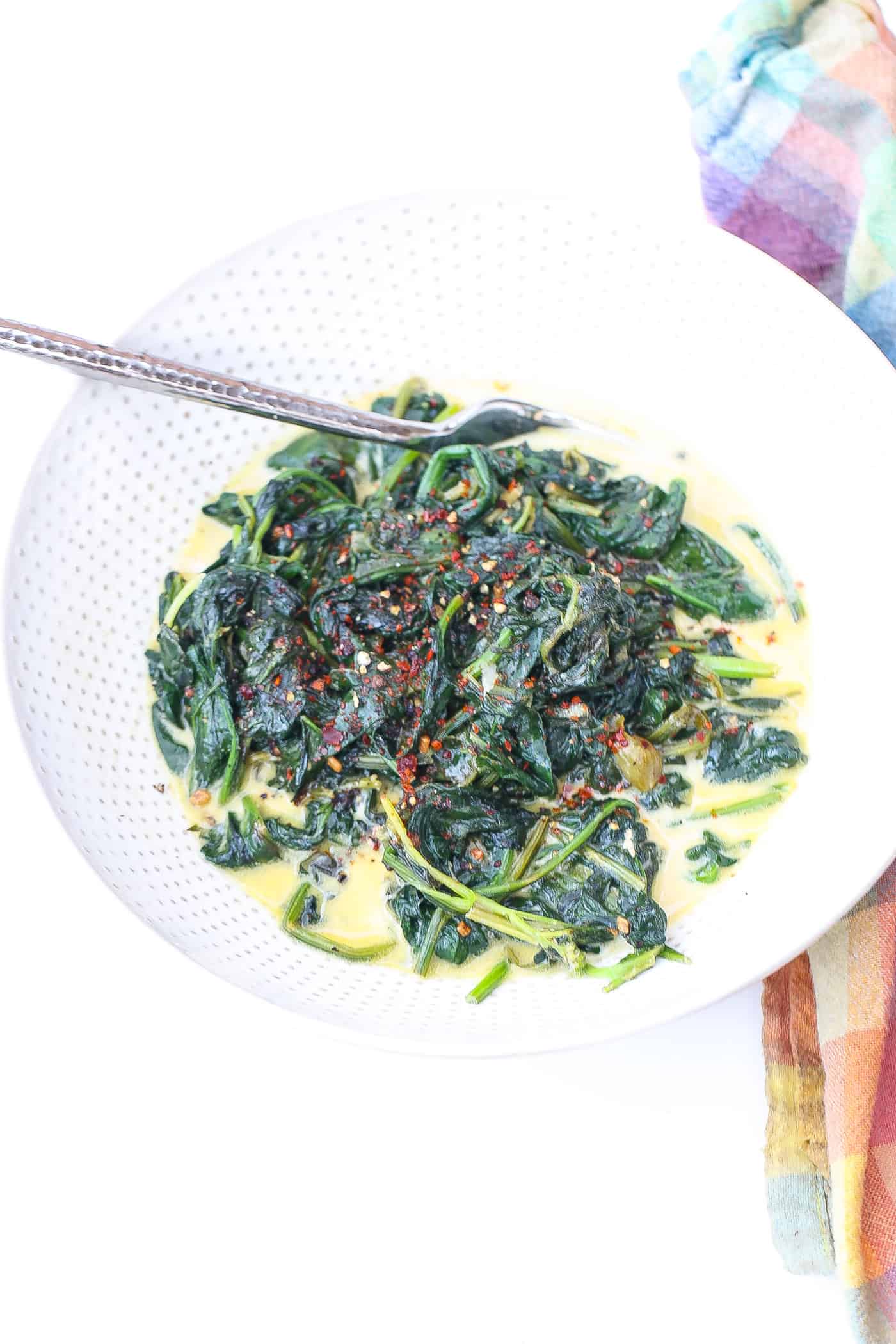 sauteed spinach in a white bowl with creamy sauce