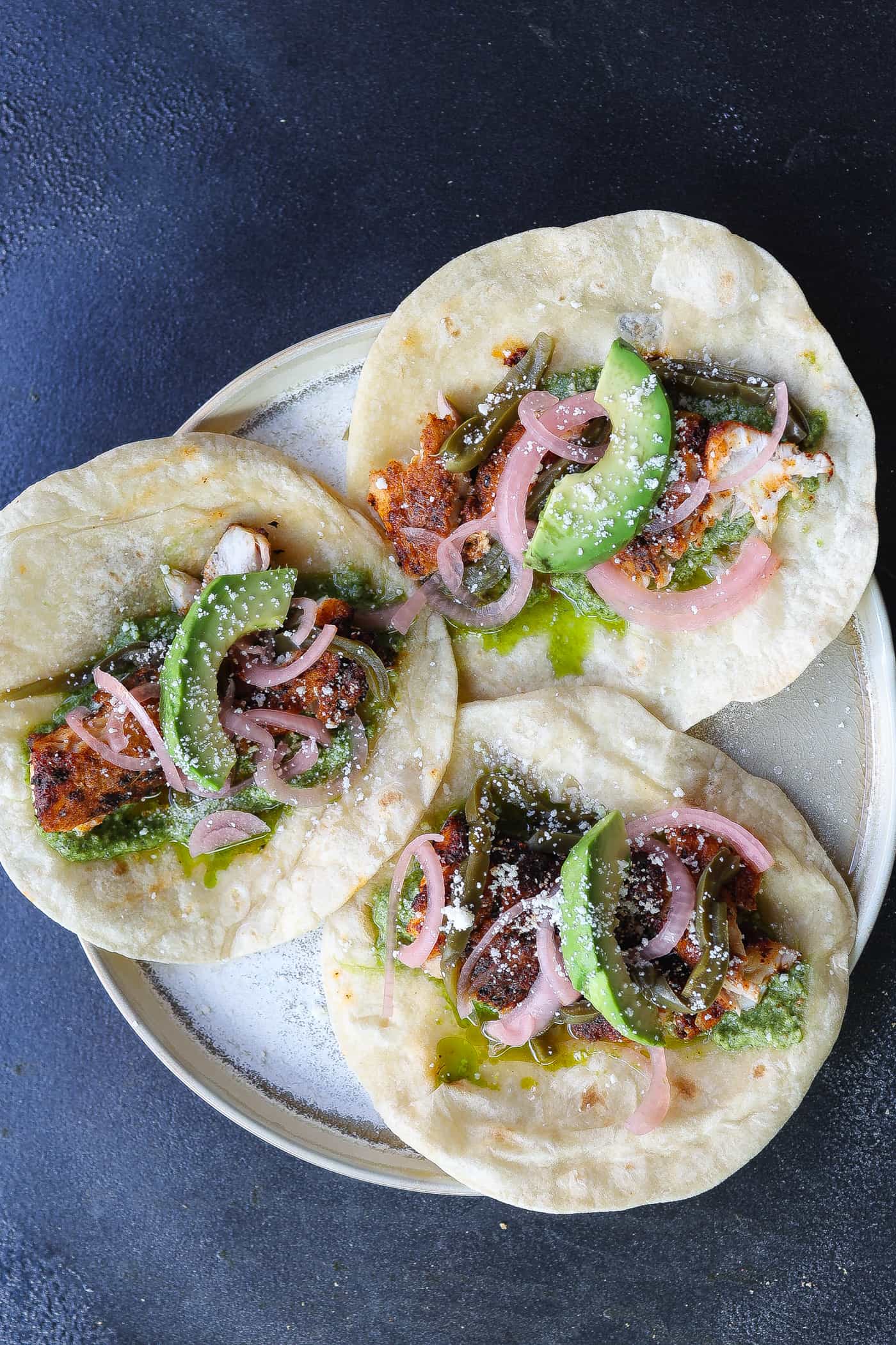 three fish tacos on a tan plate.