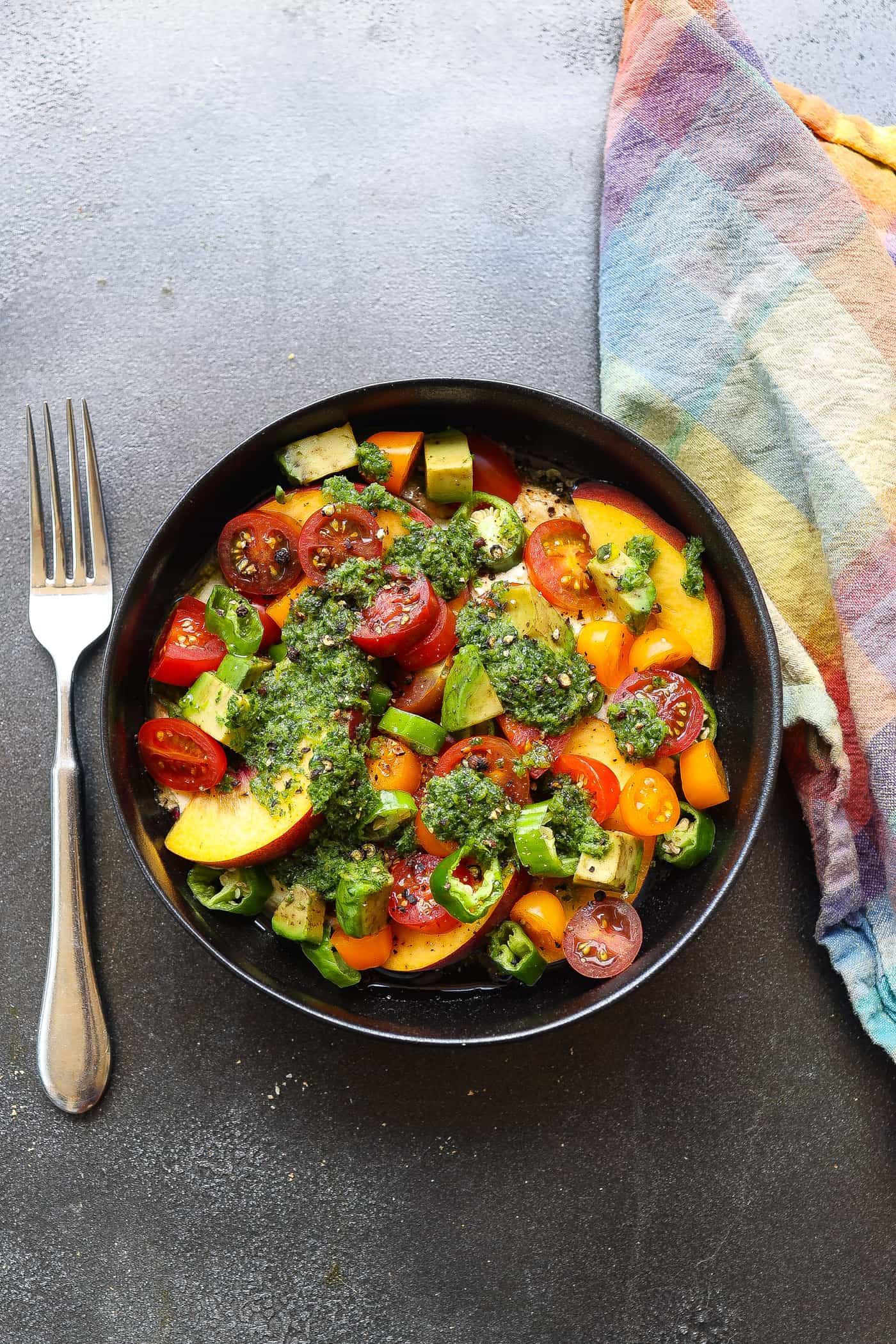 cherry tomato salad topped with green sauce in black bowl