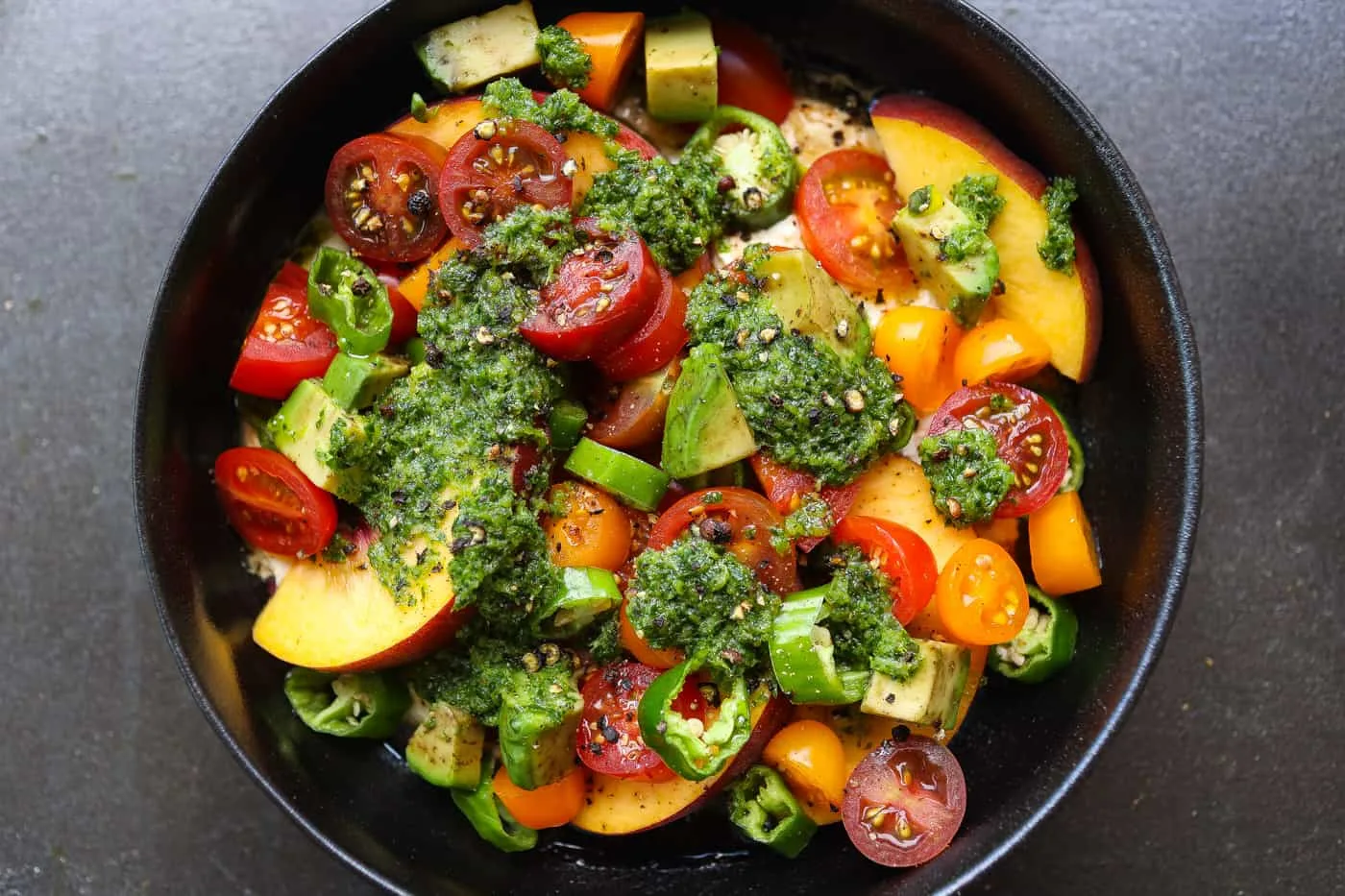 cherry tomato salad topped with green sauce in black bowl