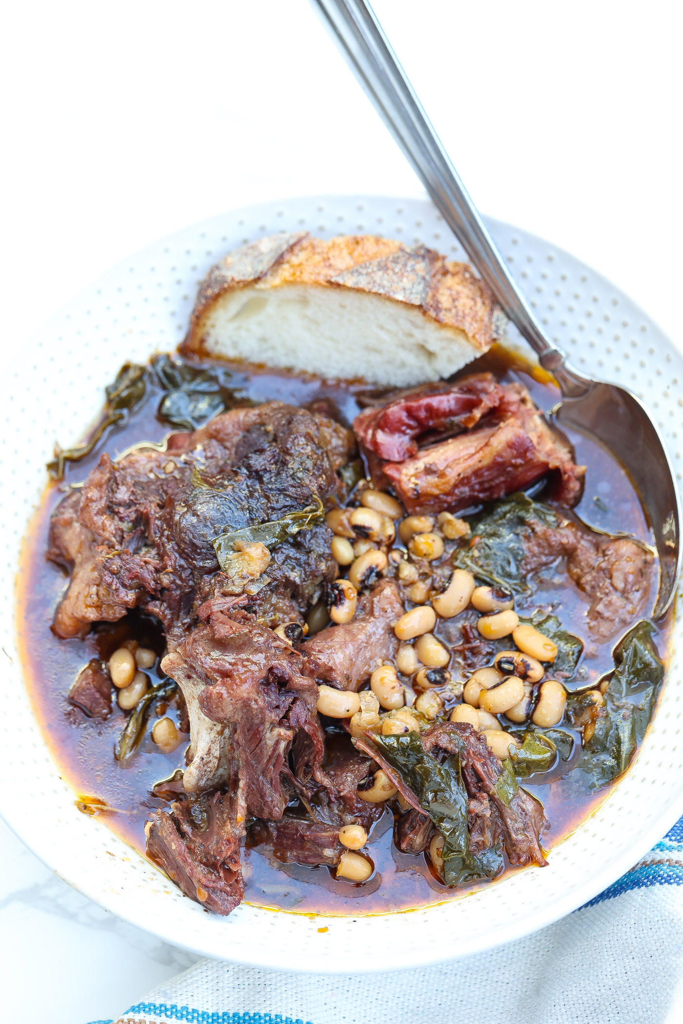 beef oxtail soup with collard greens and blackeyed peas in a white bowl