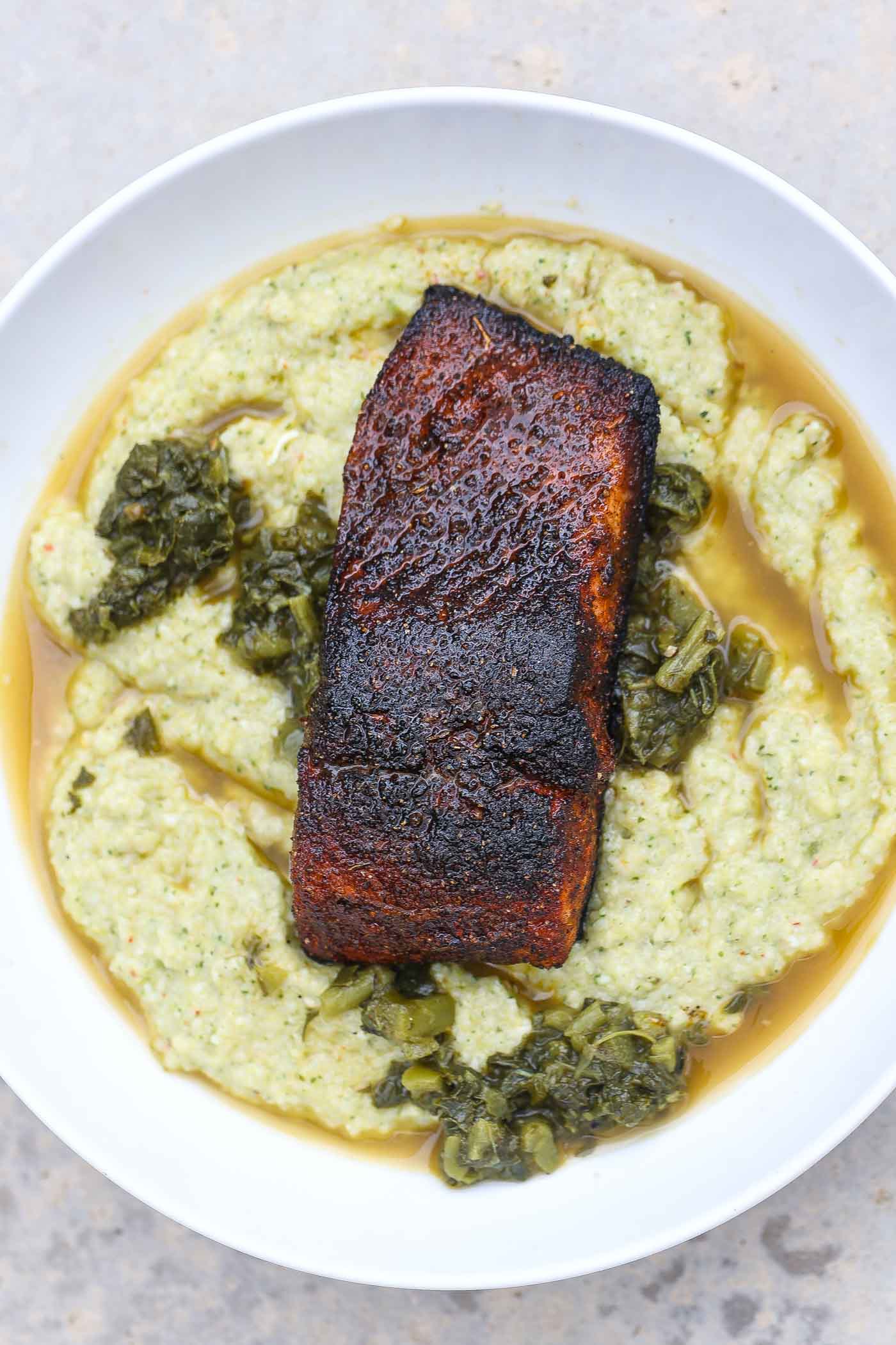 A fillet of trout with a blackened spice rub, cooked in a cast iron skillet and served over grits