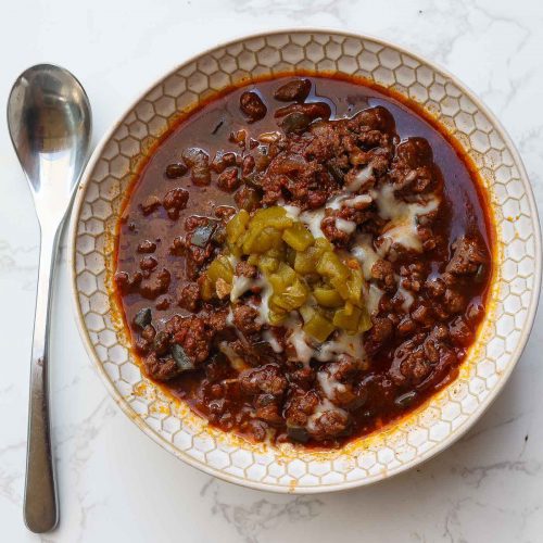 venison chili in a white bowl topped with cheese and green peppers
