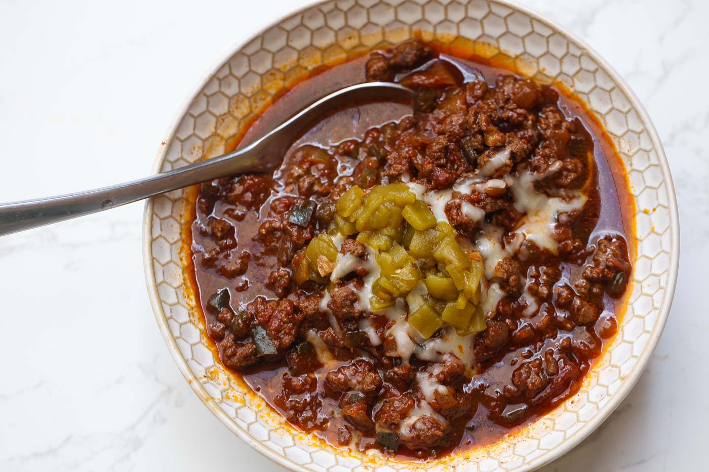 venison chili in a white bowl topped with cheese and green peppers