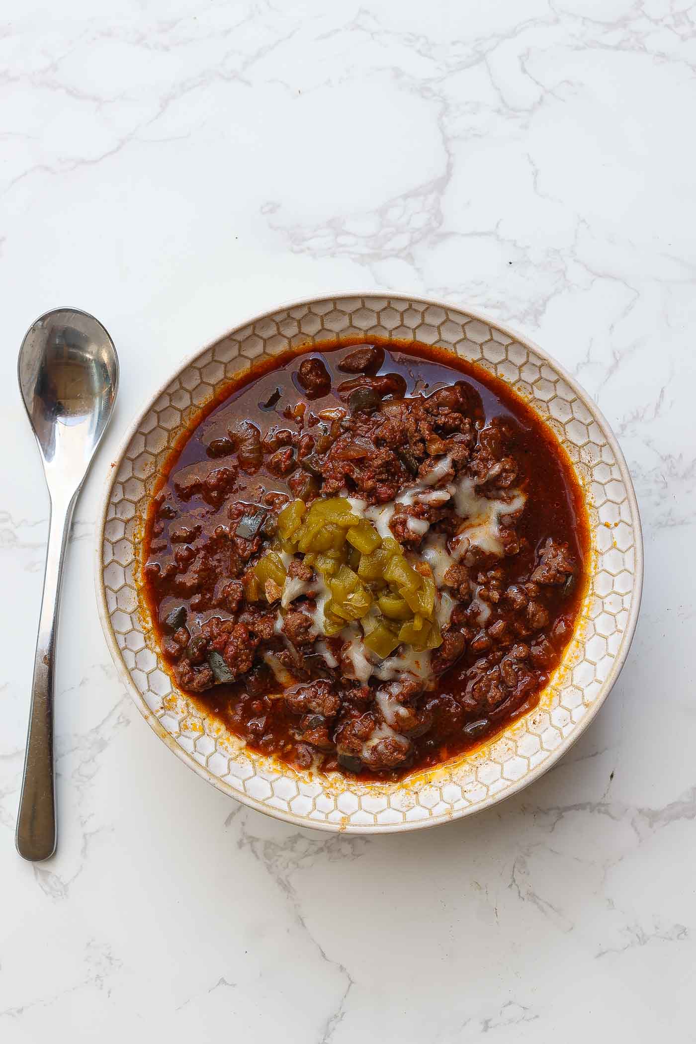 venison chili in a white bowl topped with cheese and green peppers