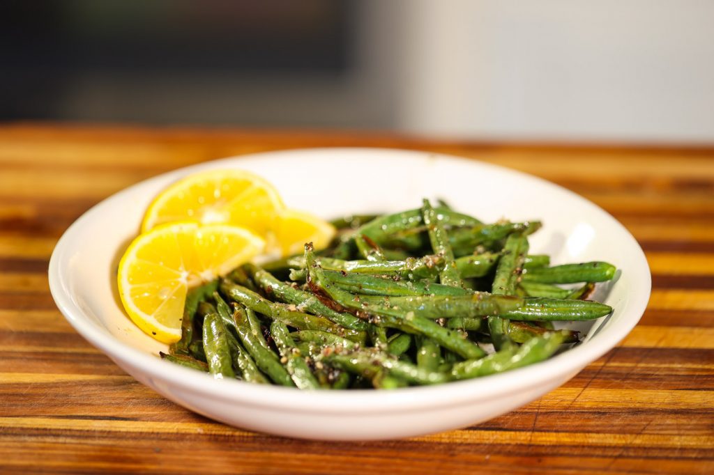 air fried green beans on a white plate with lemon slices