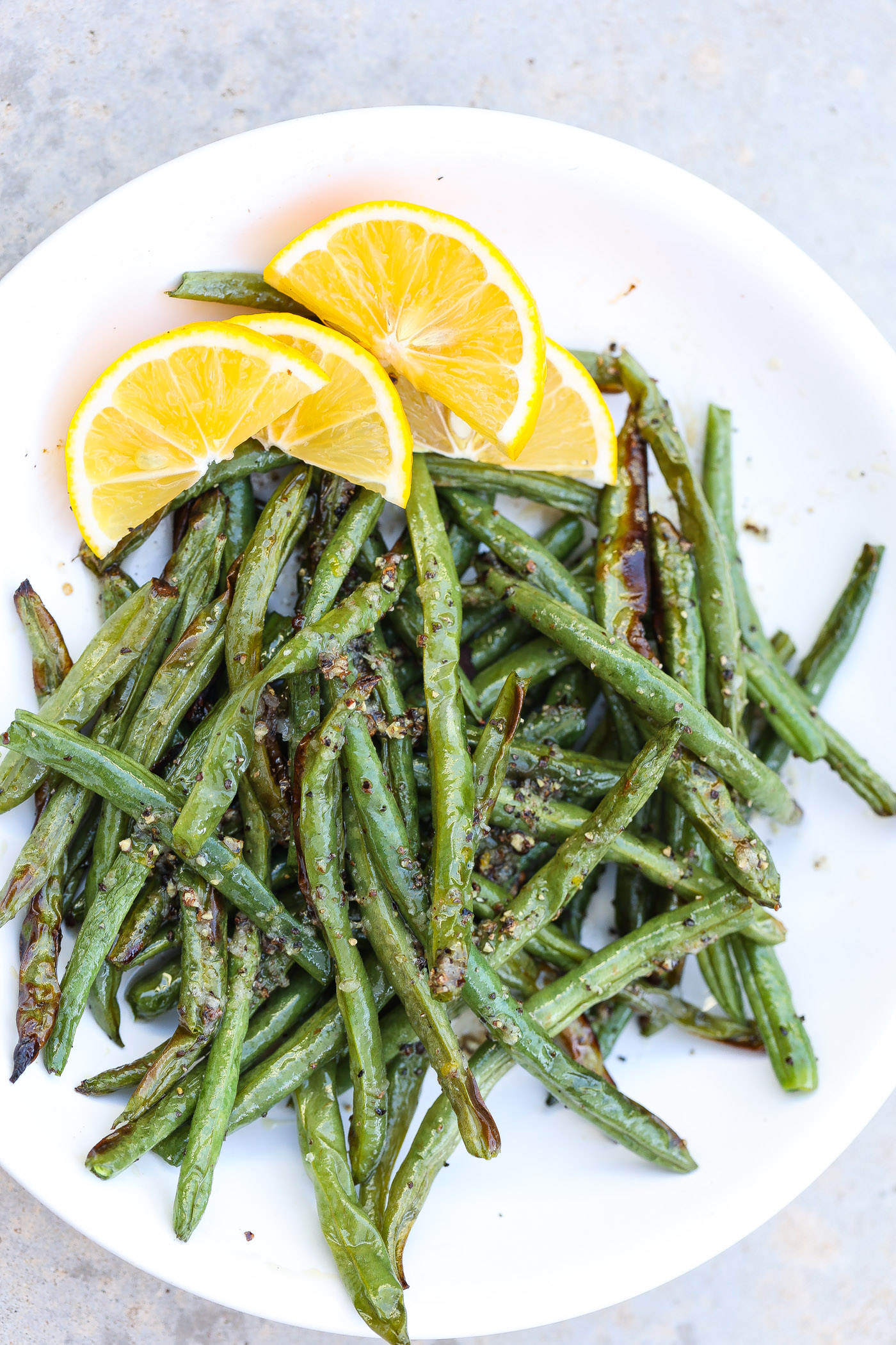 air fried green beans on a white plate with lemon slices