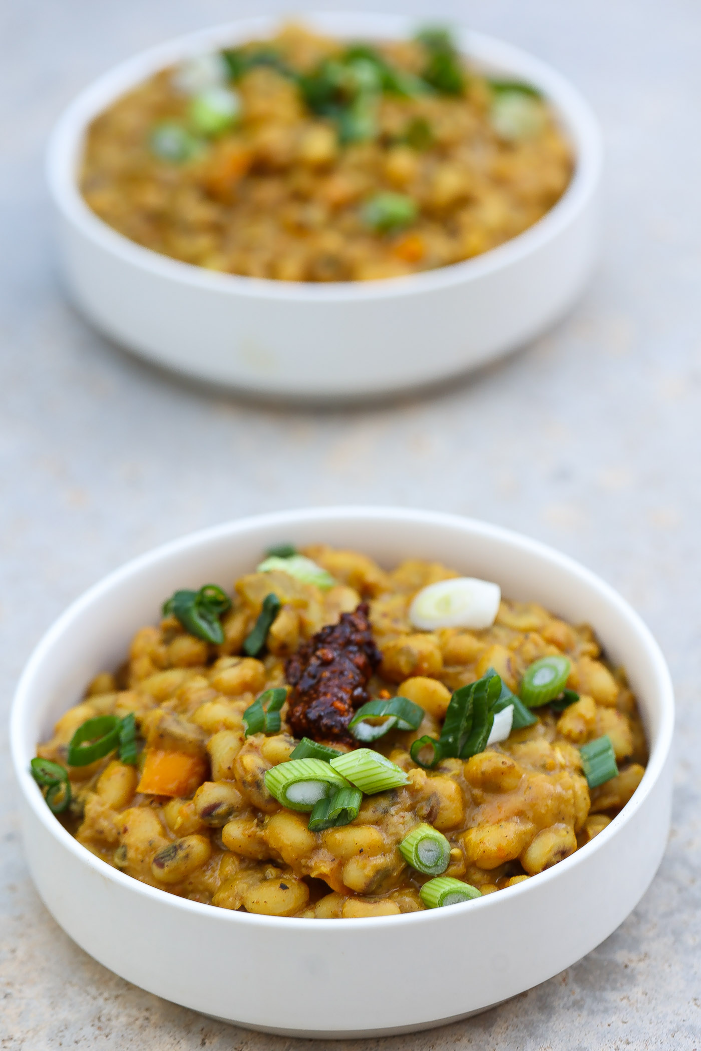 blackeyed pea curry in white bowl topped with green onions and red chili paste