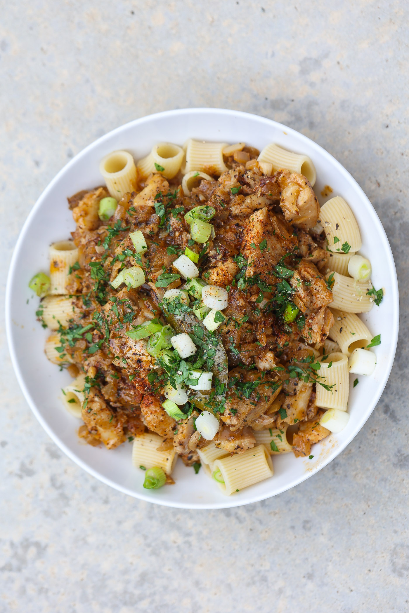 seafood pasta topped with green onions in a white bowl