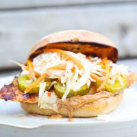 grilled chicken sandwich on a white plate topped with slaw and pickles