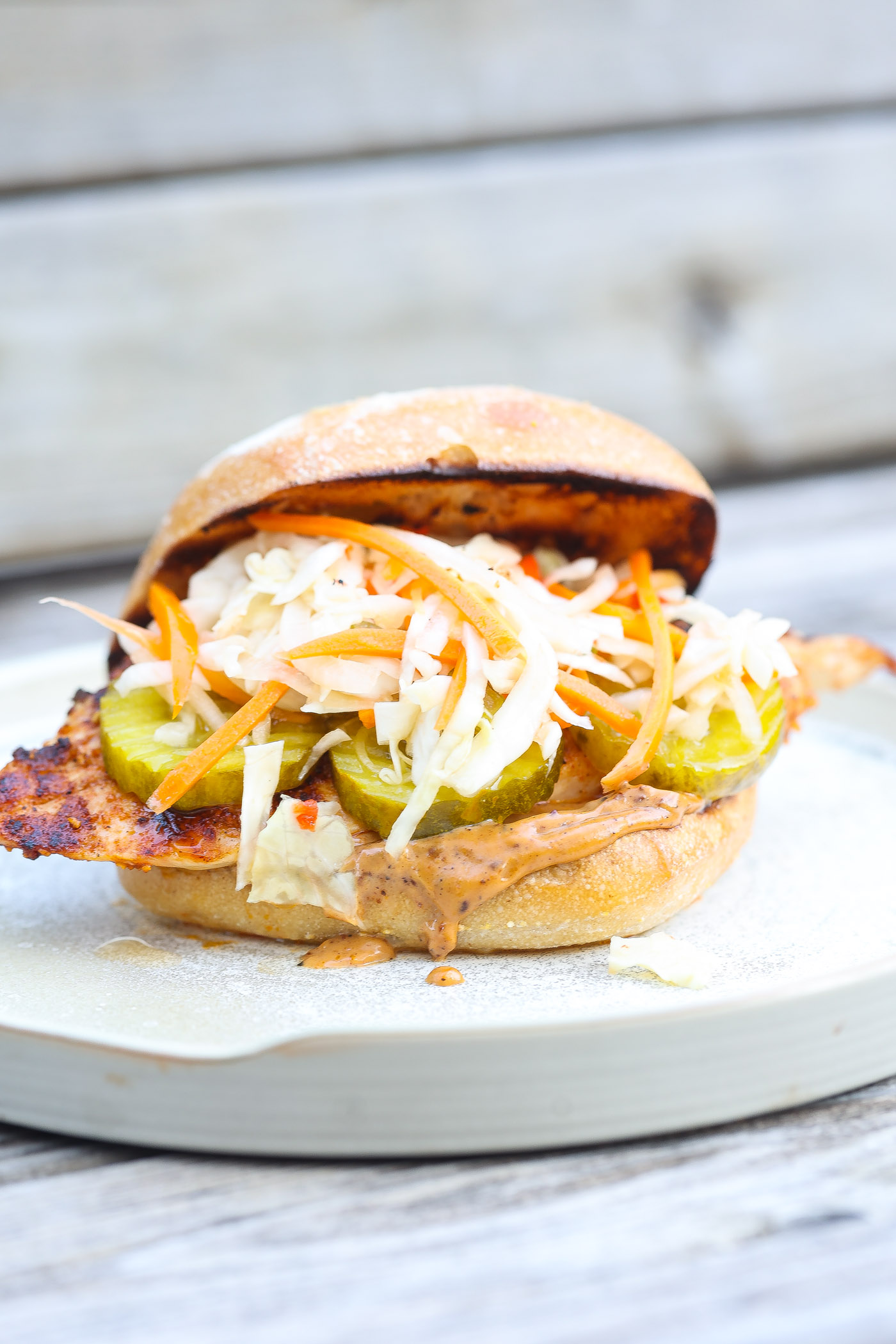 grilled chicken sandwich on a white plate topped with slaw and pickles